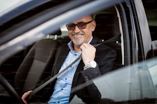幸せな成熟したビジネスマンはシートベルトを締め、車を運転する準備をしています。