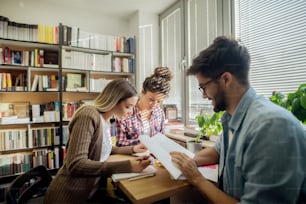 Students sitting in library and studying for exams. In background bookshelf.