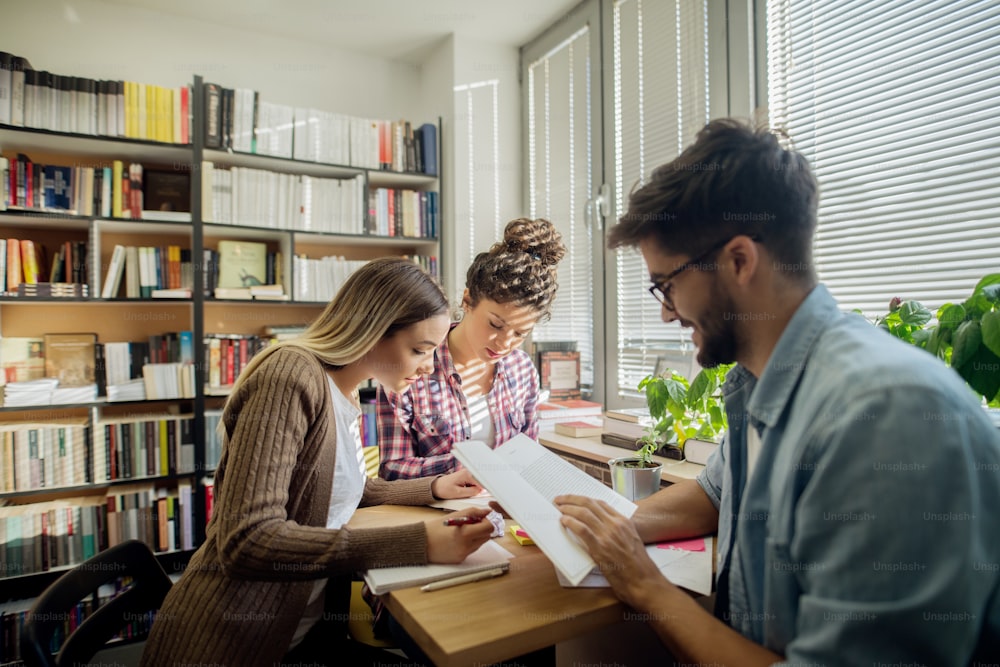 Students sitting in library and studying for exams. In background bookshelf.