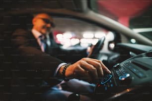 Un homme d’affaires mature en costume ajuste un volume sur sa chaîne stéréo tout en conduisant une voiture.