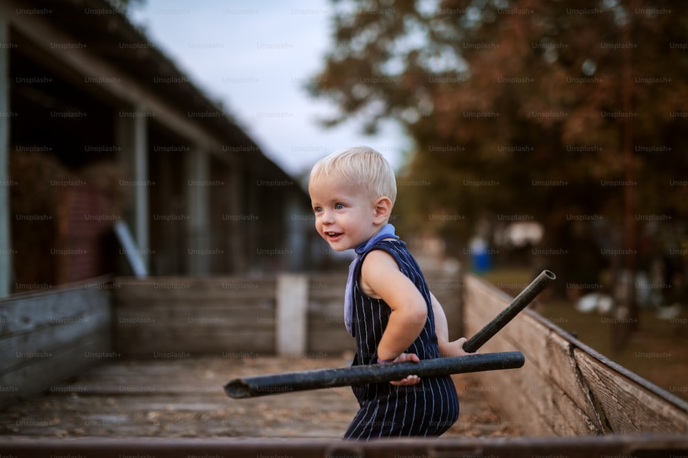 Cute cheerful small boy playing in a wooden trailer with metal pipes.