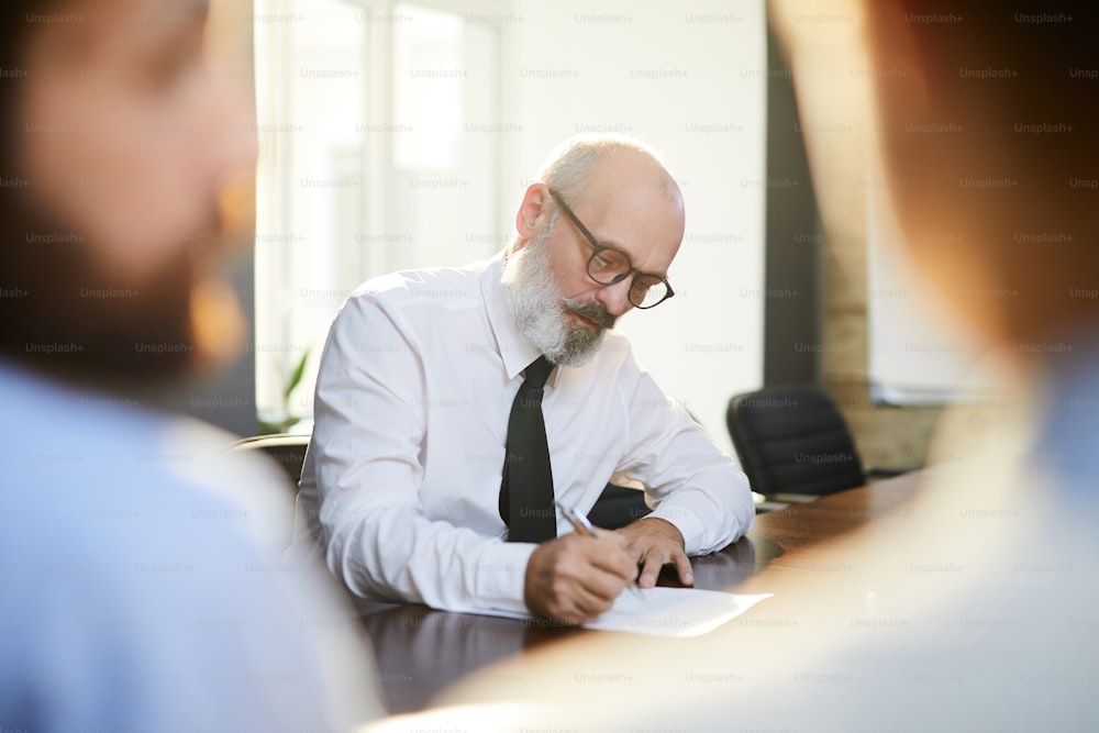 Mature applicant with grey beard reading text of contract before signing it after interview