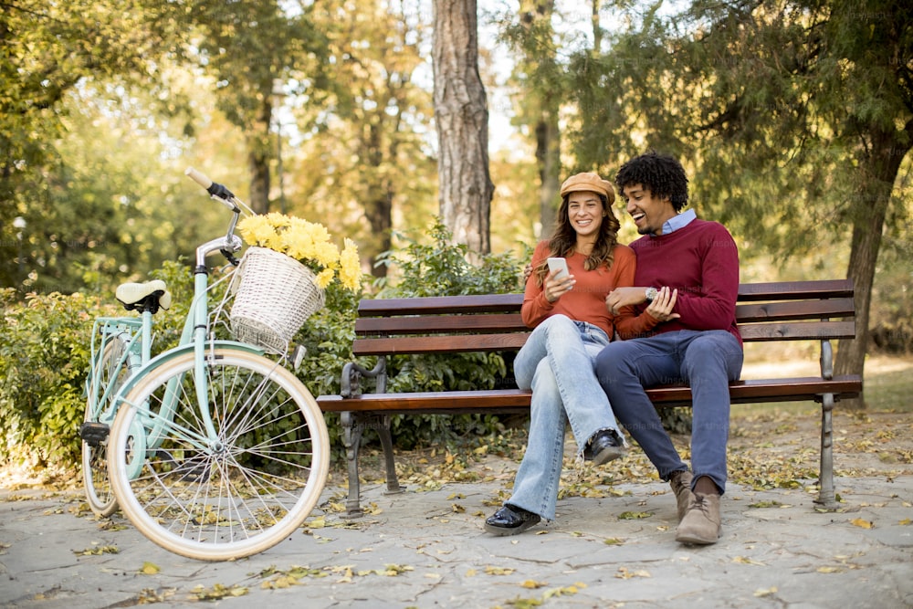 Pareja amante multiratial sentada en un banco en el parque de otoño de la ciudad