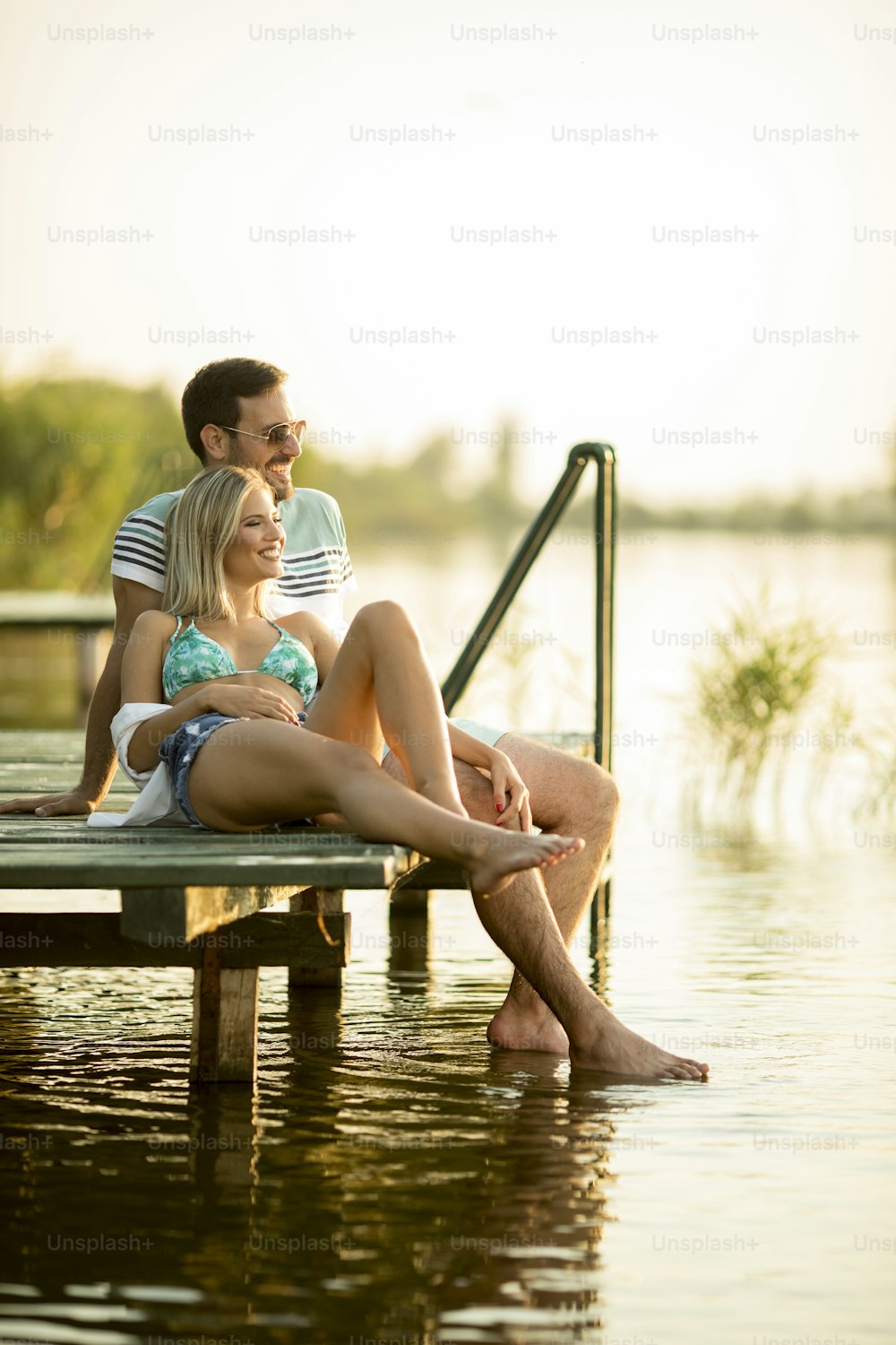 Casal romântico sentado no píer de madeira no lago em dia ensolarado
