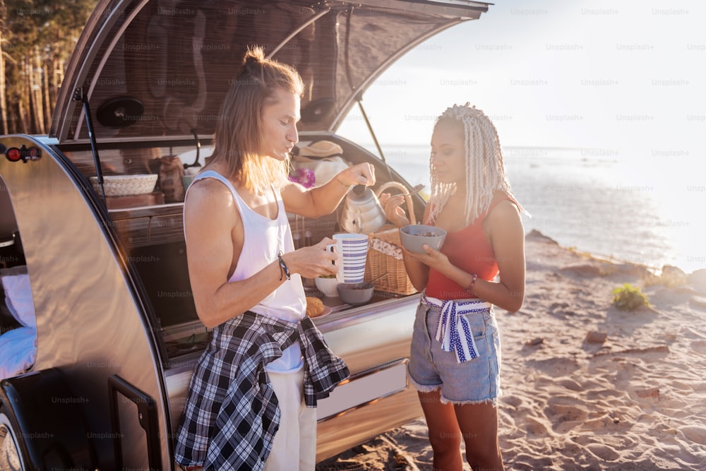 Breakfast with woman. Blonde-haired man making some tea having breakfast with his stylish woman