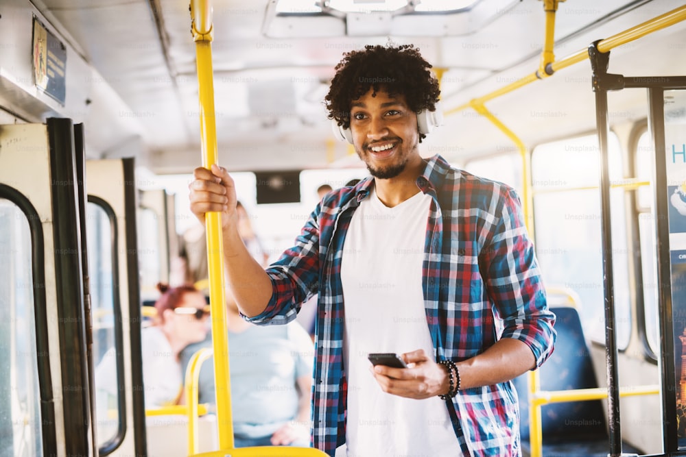 Feliz sorriu afro-americano parado em um ônibus e ouvindo a música por seu telefone.