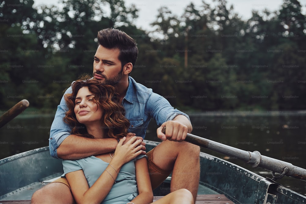 Beautiful young couple embracing and looking away while enjoying romantic date on the lake