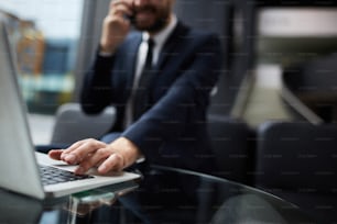 Hand des modernen mobilen Geschäftsmannes auf der Laptop-Tastatur während des Netzwerks im Büro