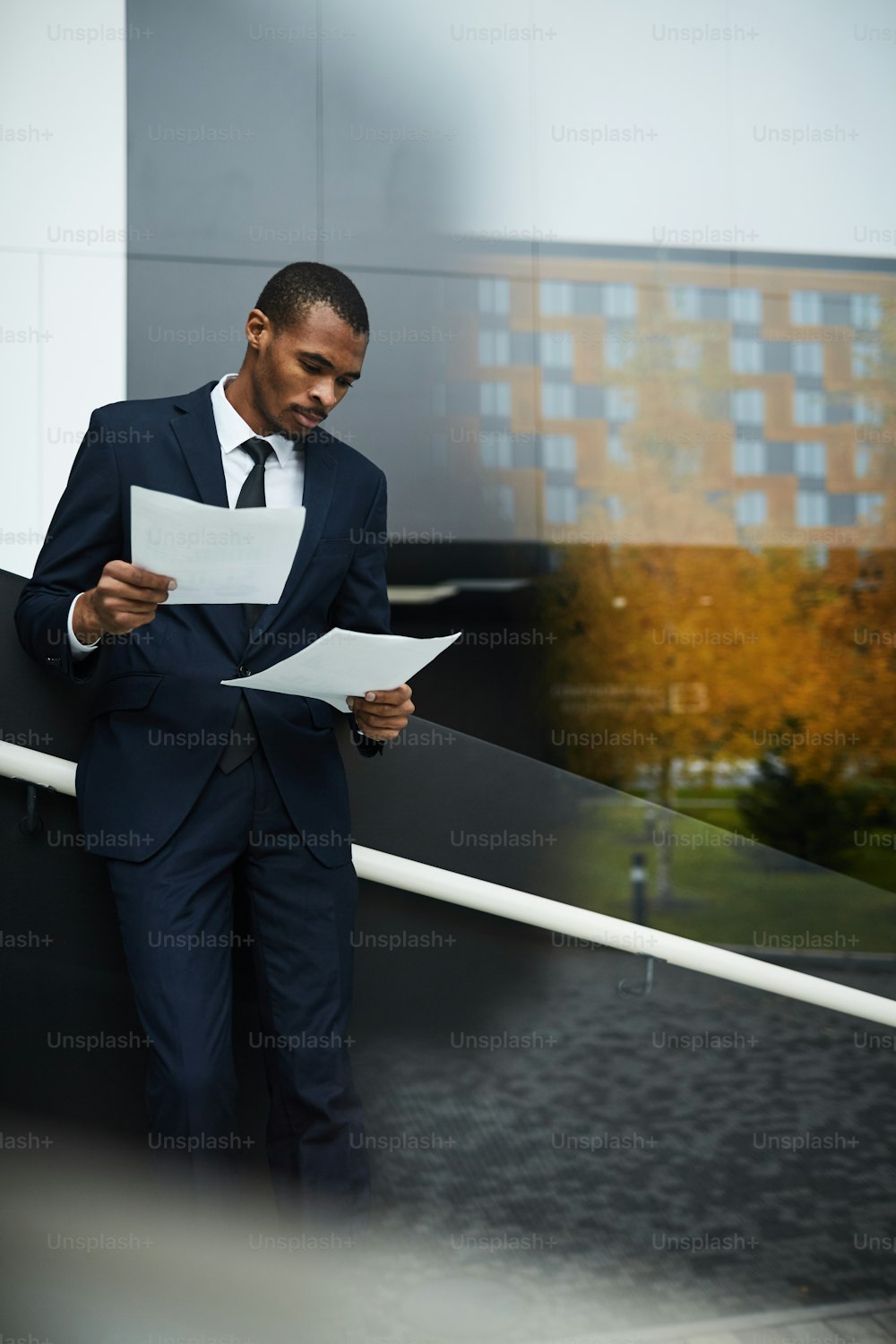 Young serious agent reading contract while standing by window in business center