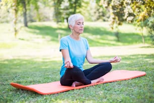 Senior woman in a lotus position   on a grass in park