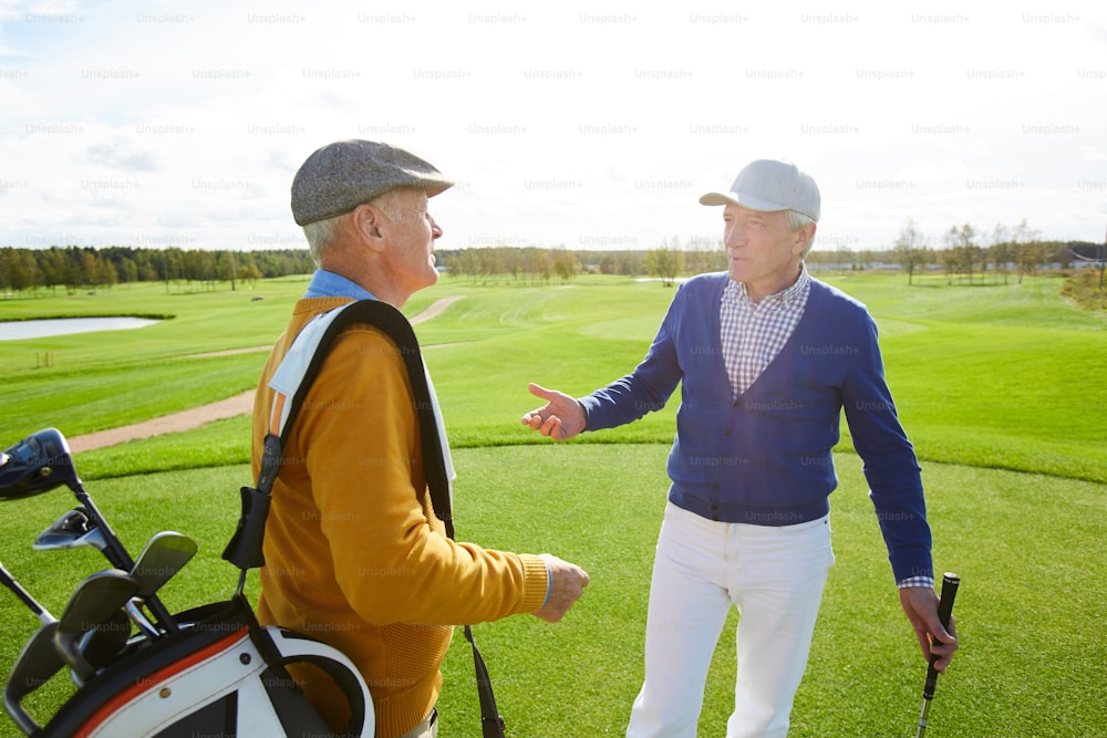 Zwei ältere Männer mit Golfschlägern unterhalten sich mitten auf der grünen Wiese vor dem Spiel im Freien