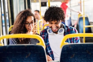 Feliz joven sonrió pareja multicultural sentada en un autobús y mirando el teléfono.