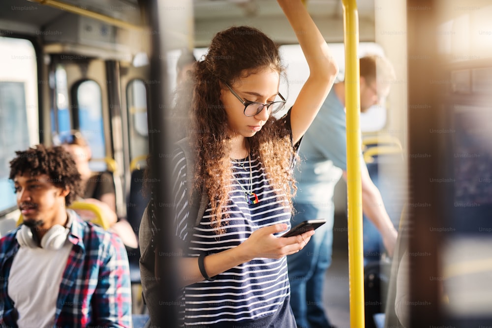 Une jeune fille mignonne se tient dans le bus et vérifie les messages sur son téléphone.