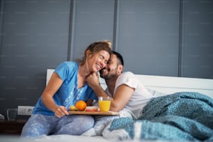 Young happy relaxed couple having breakfast together in bed. Having fun and smiling.