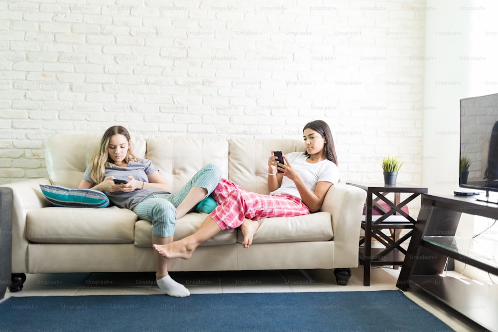 Women using their own smartphones and ignoring each other during sleepover party at home