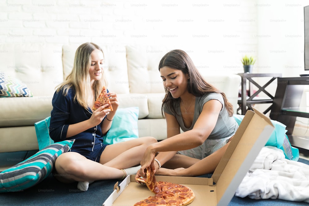 Des amies multiethniques dégustent une pizza après une soirée pyjama à la maison