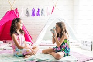 Menina pré-adolescente fotografando sua melhor amiga durante festa do pijama em casa