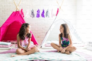 Des filles préadolescentes se regardent assises contre des tentes de tipi pendant une fête de sommeil