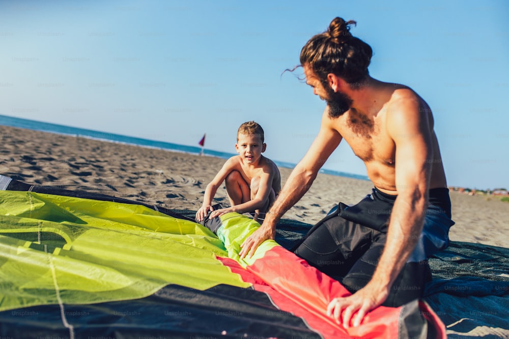 男はサーフィン用の凧道具を持ったウェットスーツを着た息子と一緒にサーファーします。