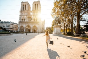 Morning view on the famous Notre-Dame cathedral with woman running on the square dispersing pigeons in Paris, France