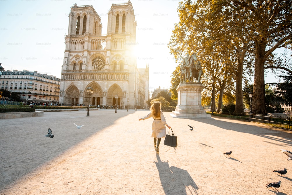 Vista mattutina sulla famosa cattedrale di Notre-Dame con la donna che corre sulla piazza disperdendo i piccioni a Parigi, Francia