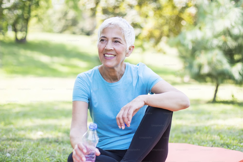 Senior sportive woman sitting on mat outside and resting after workout