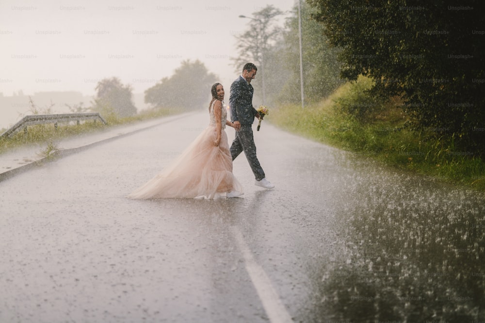 Jovem bobo acaba de casar casal cruzando estrada em dia chuvoso. Andar com roupas cerimoniais molhadas.