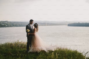 Immagine emotiva di una coppia appena sposata in piedi nel campo e che si bacia. Fiume sullo sfondo. Obiettivi di coppia.