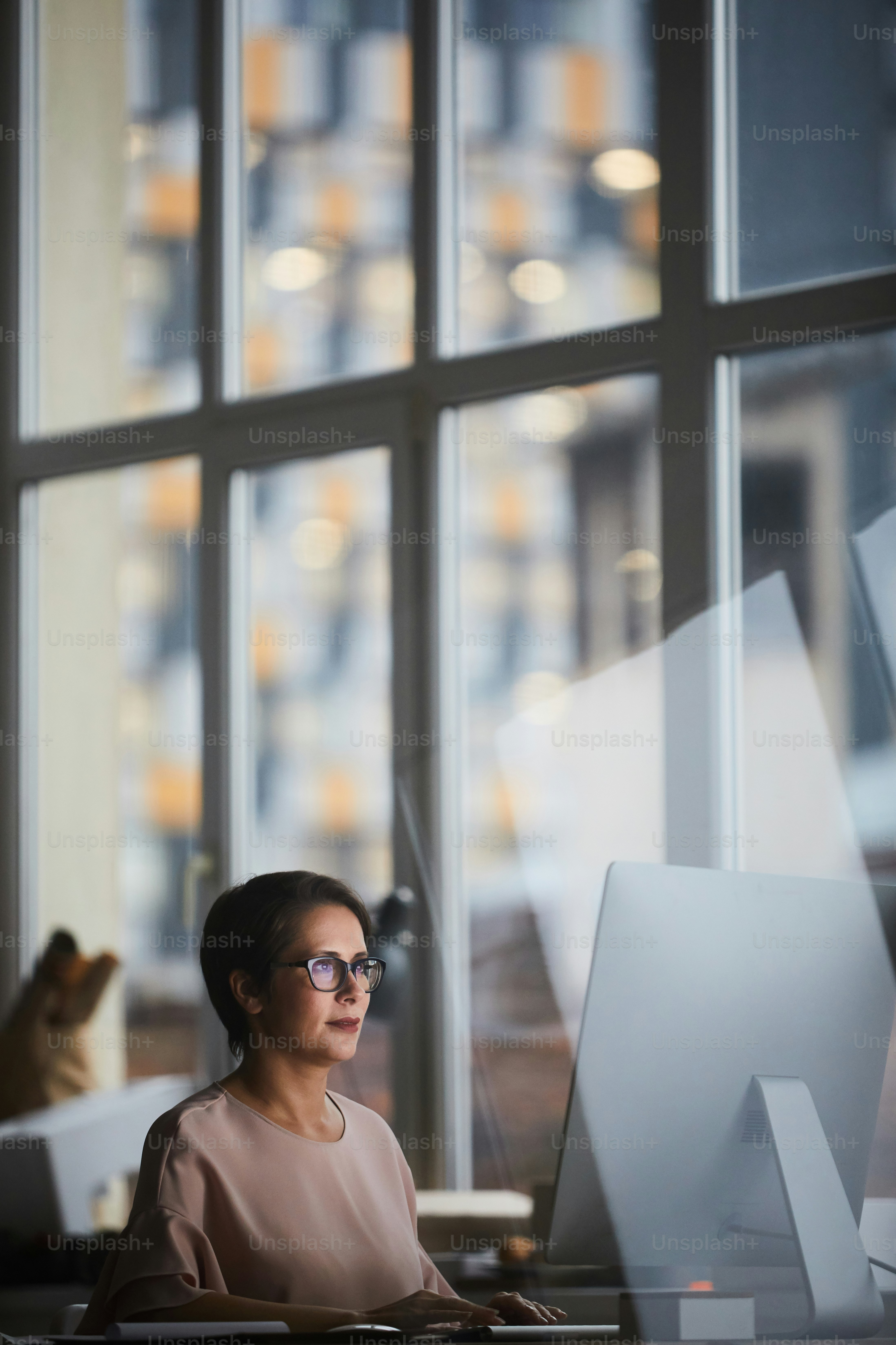 Young modern businesswoman sitting by table in office and browsing in the net