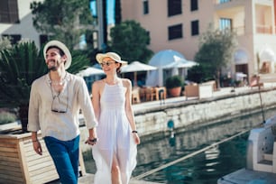 Giovani coppie felici che camminano dal porto di una località balneare turistica con barche a vela sullo sfondo
