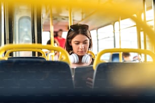 Girl with headphones sitting in a public transportation and watching at tablet.