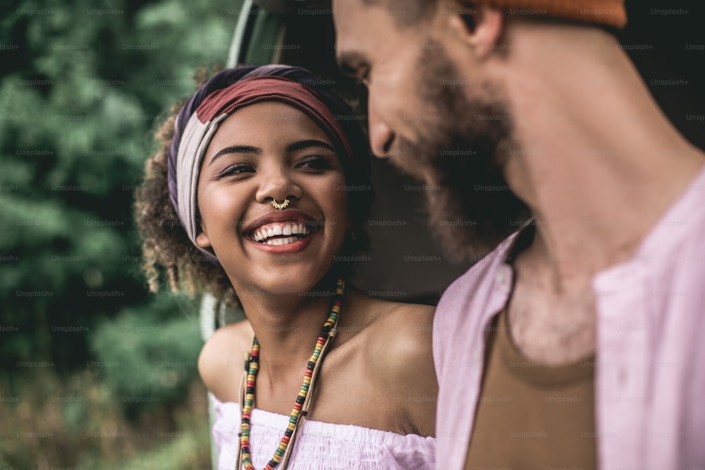 Concept of hippie lifestyle and travel. Close up portrait of cheerful afro-american lady and hipster male looking happy to each other
