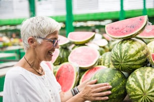 Retrato da mulher sênior que compra melancia no mercado