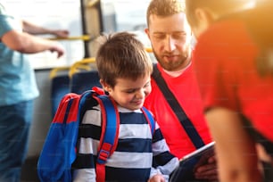 Father and son in a bus looking at tablet and talking.