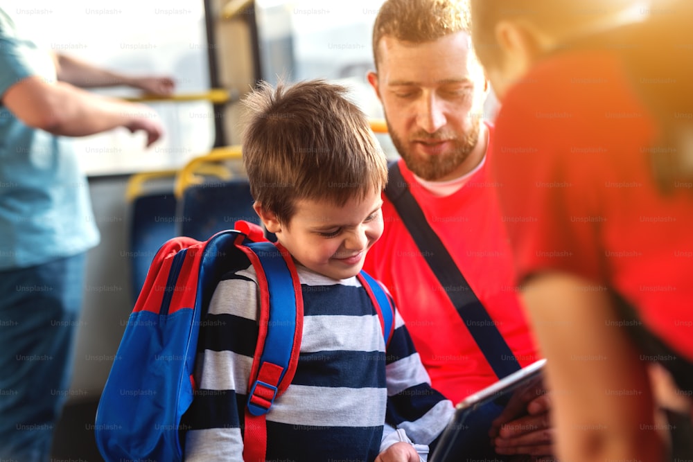 Vater und Sohn in einem Bus, schauen auf das Tablet und reden.
