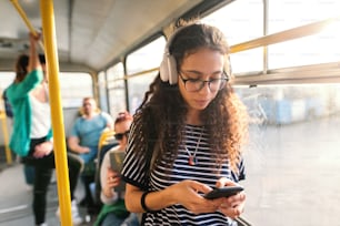 Schöne gemischtrassige Frau, die Musik hört, ein Smartphone benutzt und in öffentlichen Verkehrsmitteln steht.