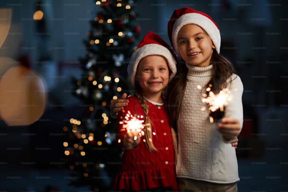 Cheerful little girls in xmas attire holding burning bengal lights on Christmas night