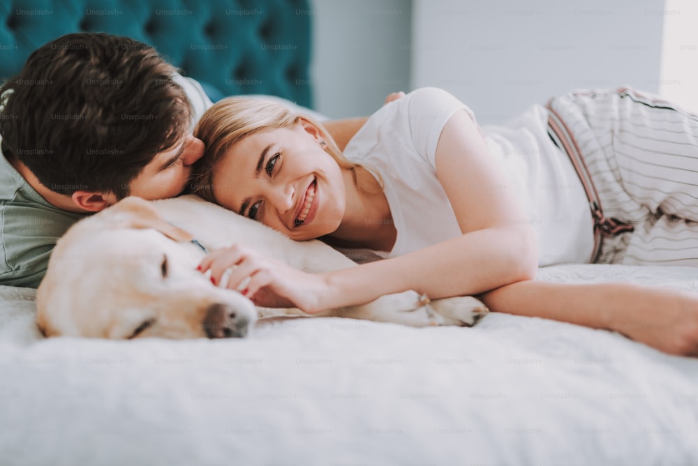 Lächelnde attraktive Frau, die sich mit ihrem Freund im Bett ausruht, während sie einen angenehmen Morgen genießt