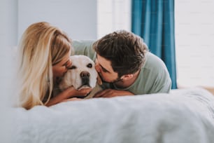 Agradable pareja joven descansando en la cama mientras besa a su perro