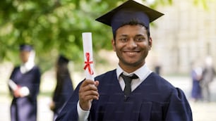 Pós-graduação em vestimenta acadêmica e boné mostrando diploma e sorrindo, educação