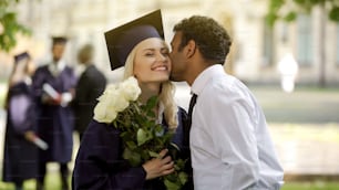Namorado carinhoso dando flores para sua namorada graduada e beijando-a