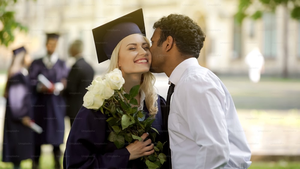 思いやりのあるボーイフレンドが卒業生のガールフレンドに花を贈り、彼女にキスをする