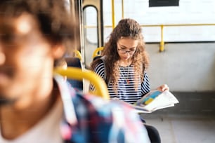 Menina mestiça lendo jornal e sentada enquanto espera ônibus para começar. Técnica de foco de imagem.