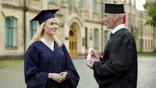 Chancellor of university giving diploma to graduating student, successful future