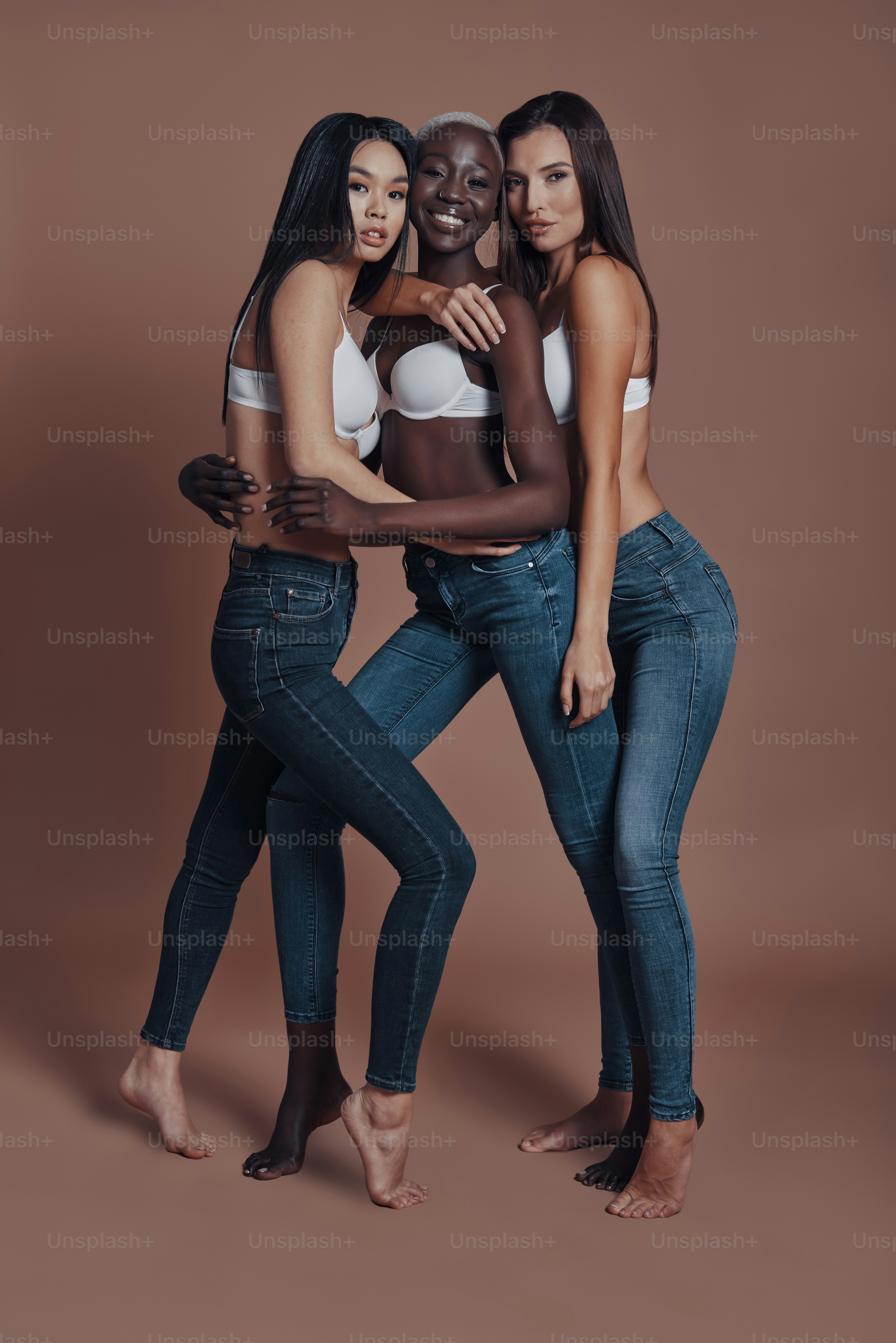 Full length of three attractive young women looking at camera and smiling while standing against brown background