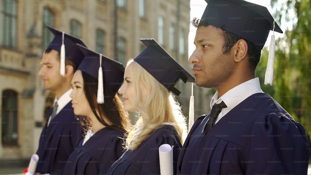 Graduate students in academic regalia standing in line and listening to speech