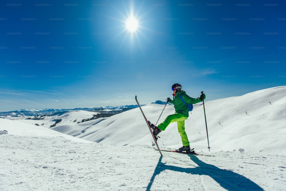 Skier standing with one raised leg on a ski slope at a sunny day and looking somewhere