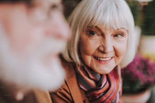 Close up portrait of joyful old woman looking at gentleman with love and smiling. Focus on female pensioner