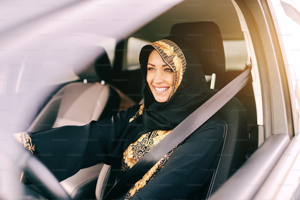 Belle femme musulmane avec un sourire aux dents conduisant une voiture.