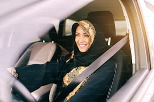 Beautiful muslim woman with toothy smile driving car.